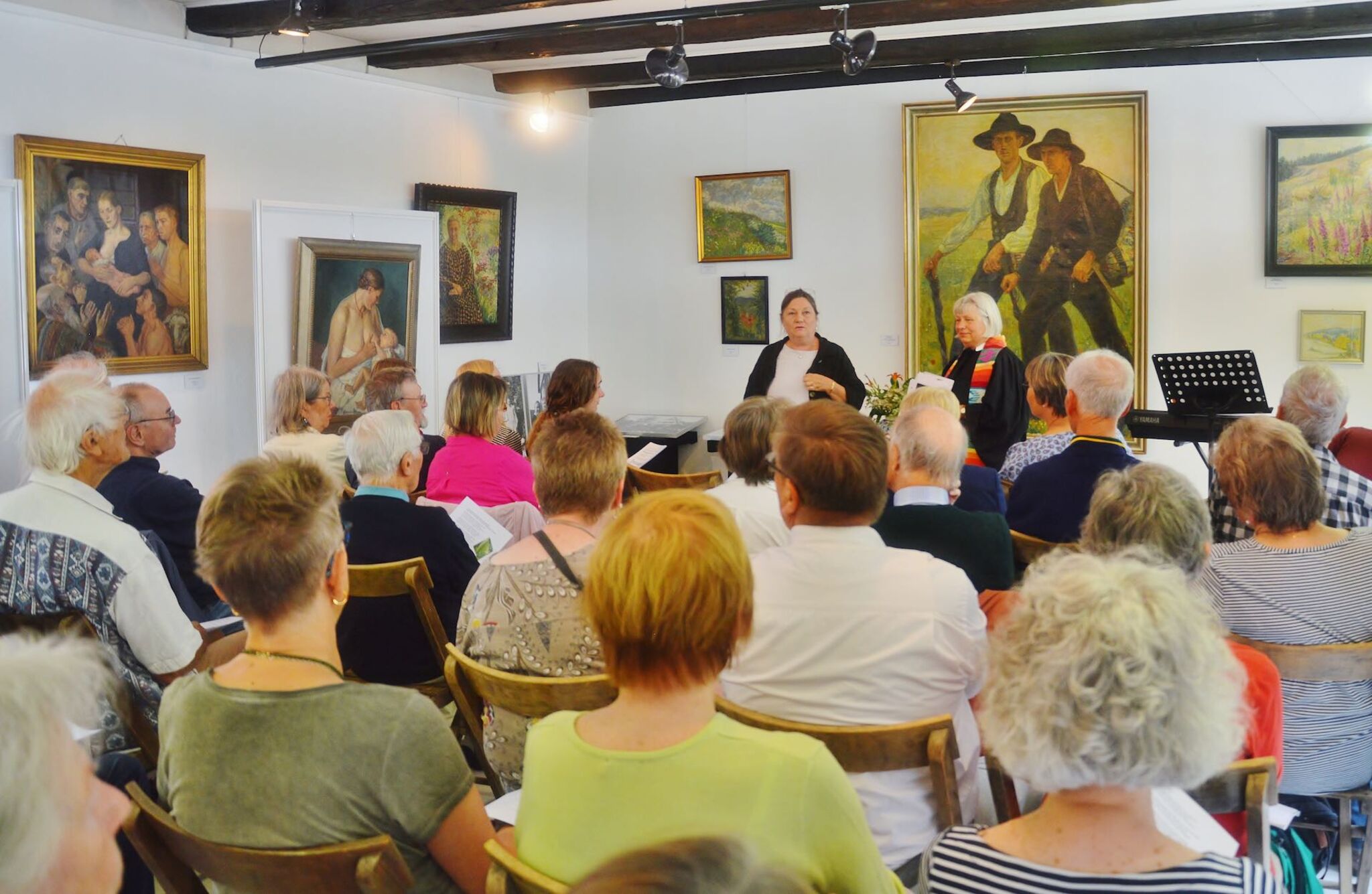 Auf dem Bild ist das Museum in Osterode zu sehen. Menschen feiern mit einer Pastorin darin Gottesdienst. An der Wand des Museums hängen Bilder, die vom Leben in der Region erzählen.