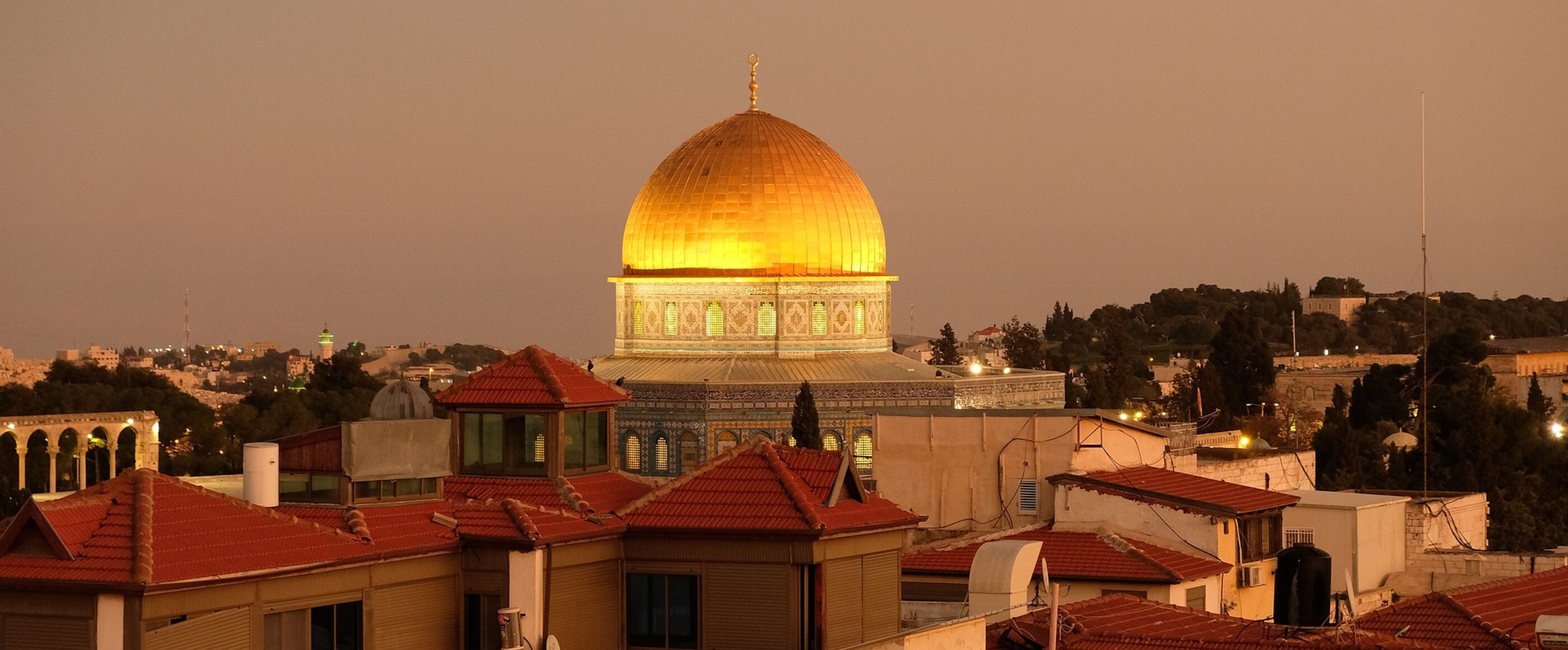 Die goldene Kuppel des Felsendoms ist zu sehen, umgeben von der Stadt Jerusalem. Das Dach des Felsendoms schimmert golden im Sonnenuntergang.