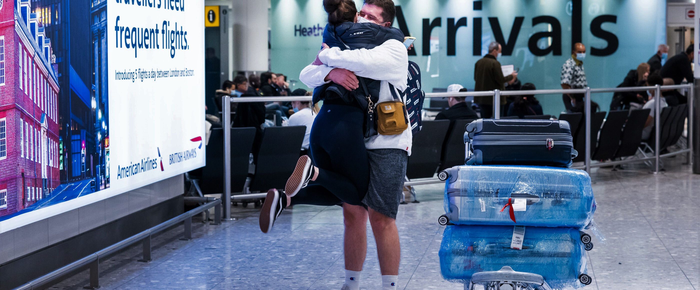 In einer Flughafen-Ankunftshalle umarmen sich ein Mann und eine Frau.