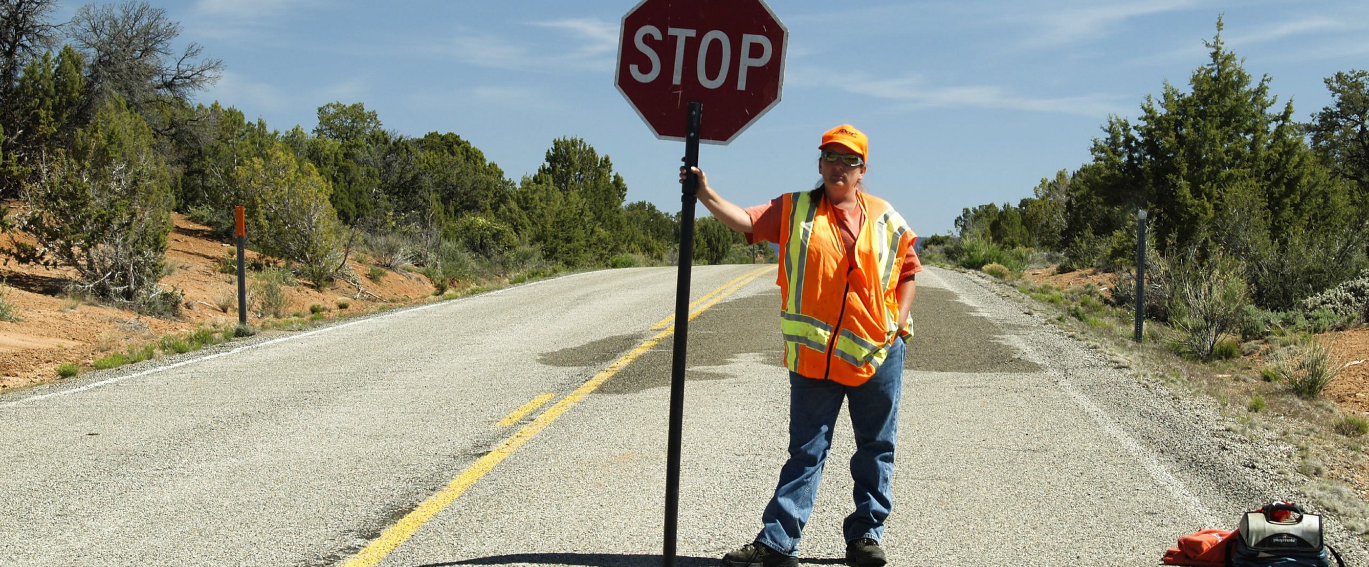 Ein Mann mit Bauarbeiter-Weste steht mit einem Stop-Schild auf einer Straße.