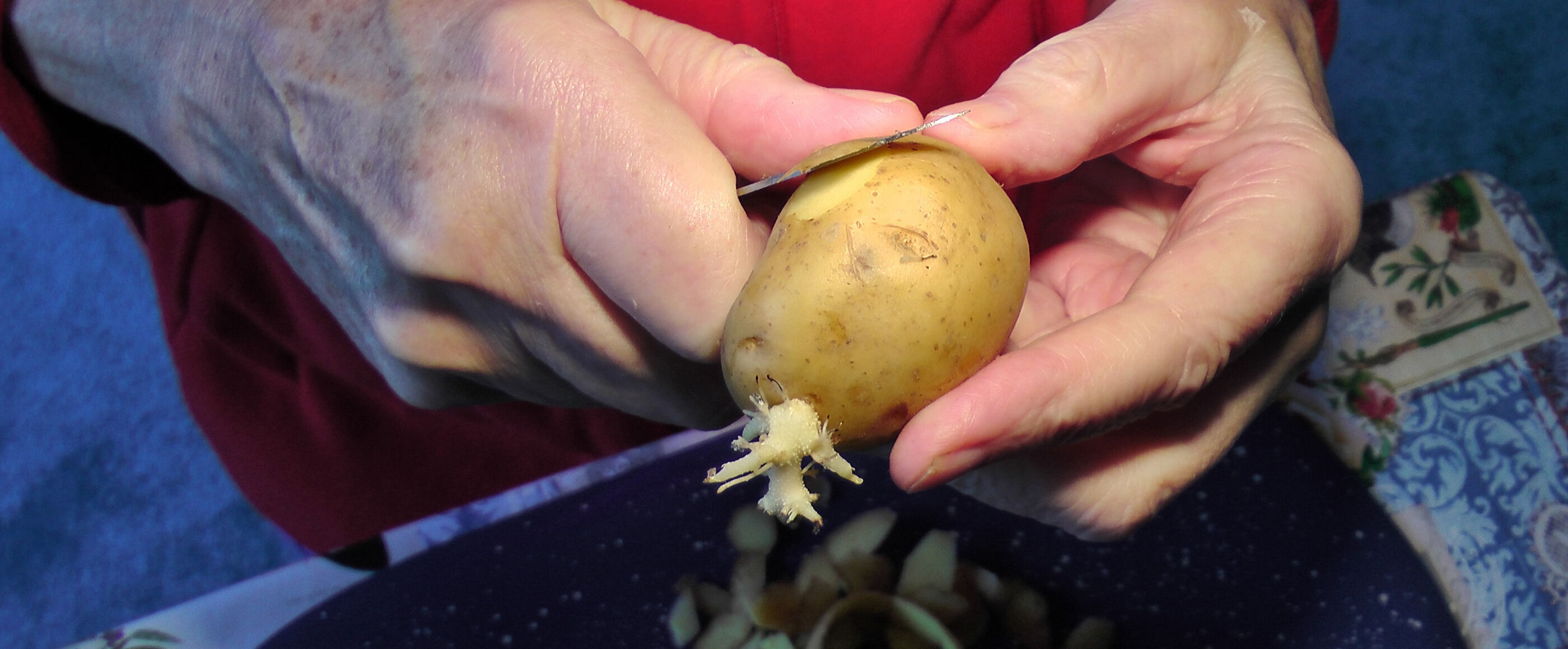 Zwei Hände schälen eine Kartoffel mit einem Messer