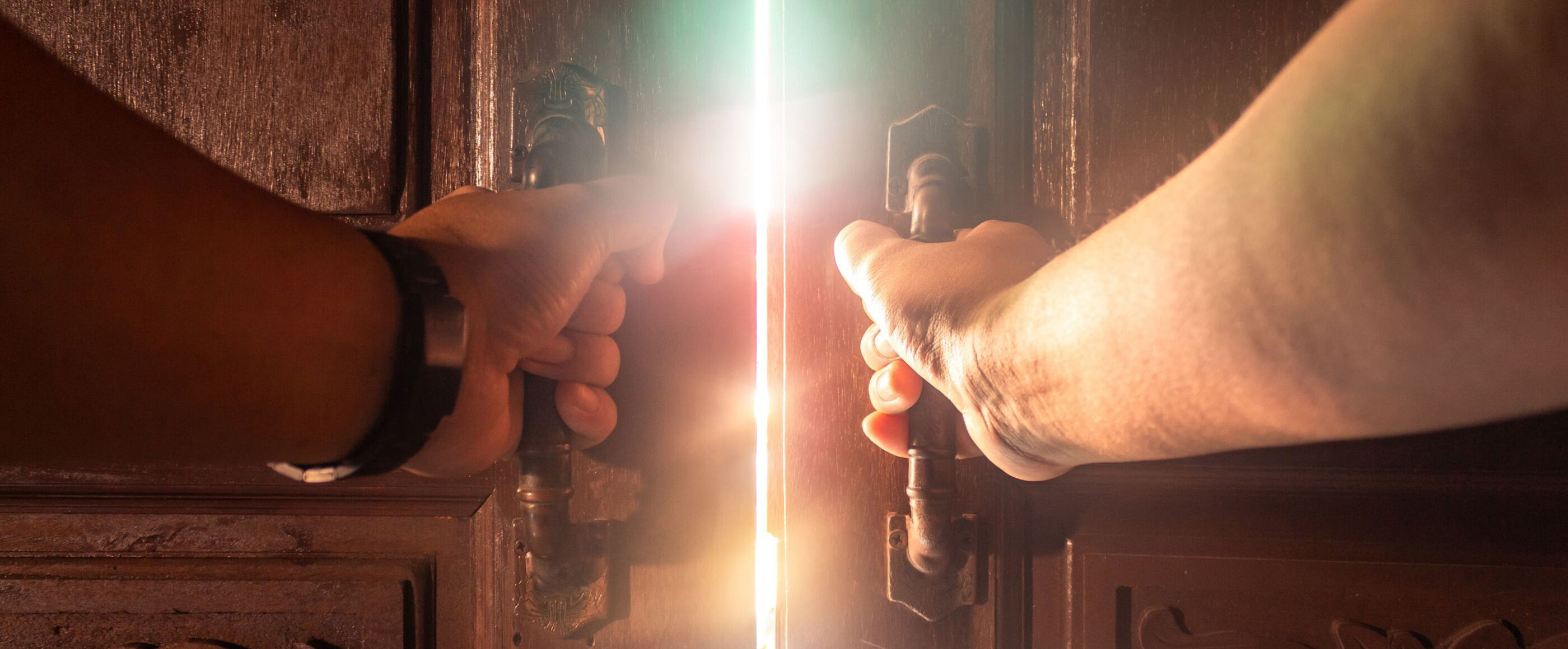 Zwei Hände öffnen eine Tür. Durch den offenen Türspalt dringt Sonnenlicht.