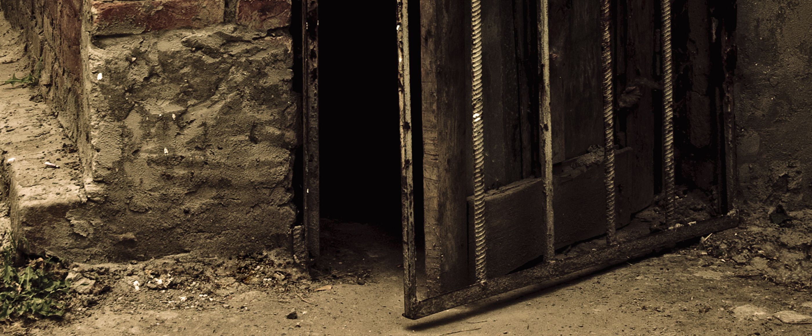 Eine leicht geöffnete Holztür in einer Steinmauer führt in einen dunklen Gang
