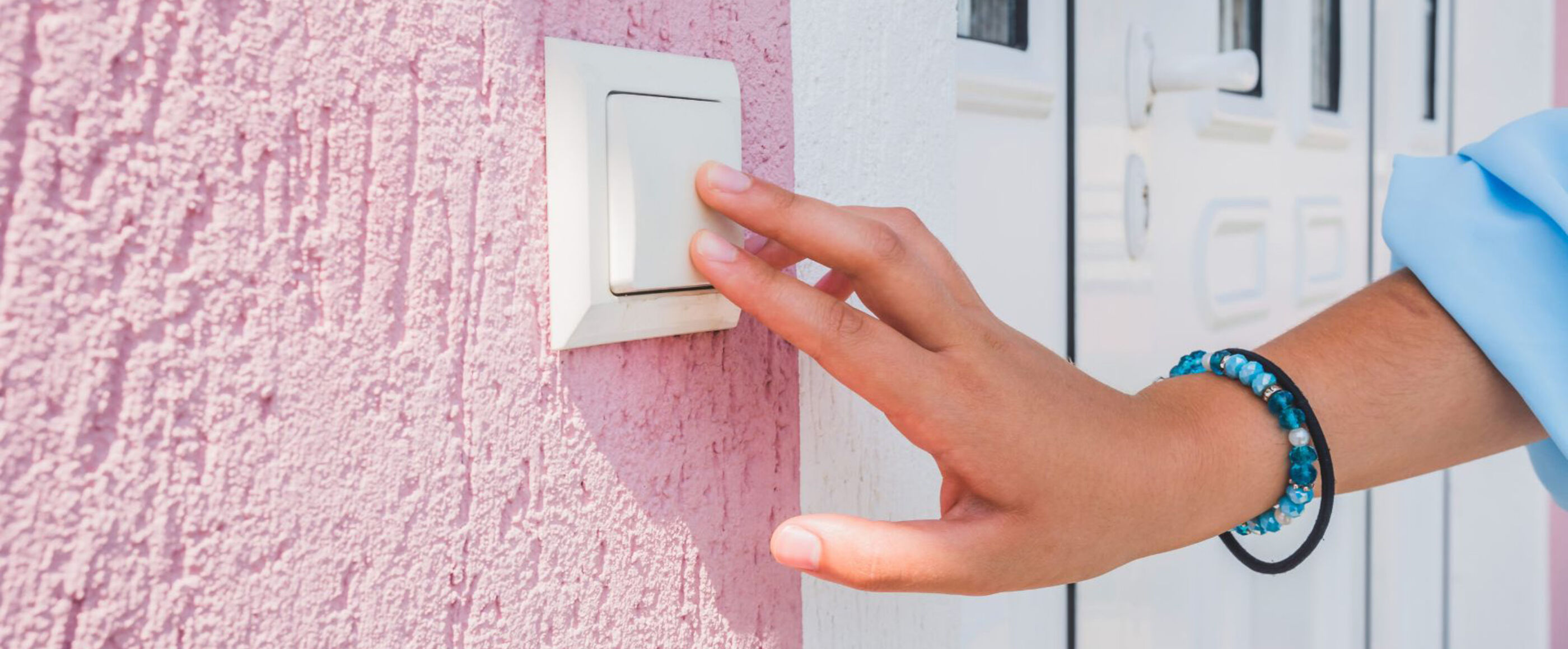 Ein Finger drückt auf einen Klingelknopf an einer rosa Hauswand.