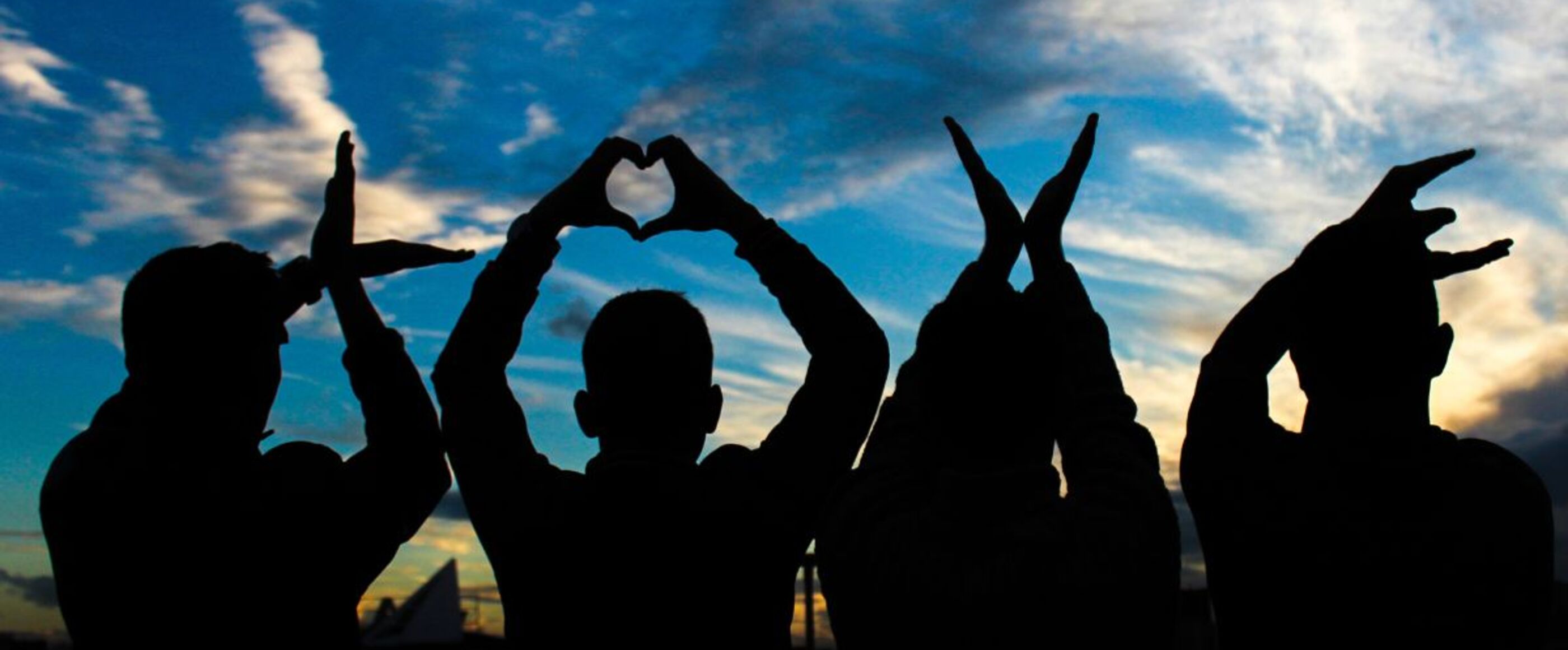 Vier Personen heben sich als Schatten gegen den Himmel ab und formen mit den Händen das Wort "Love"