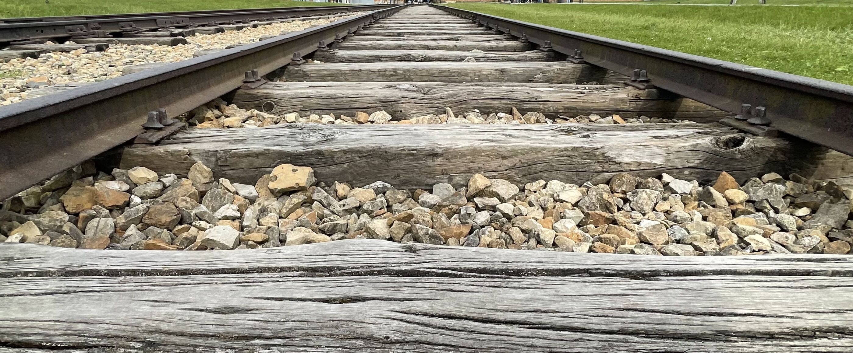 Blick aus der Froschperspektive über Gleise, die zu einem großen Gebäude führen - dem KZ Auschwitz.