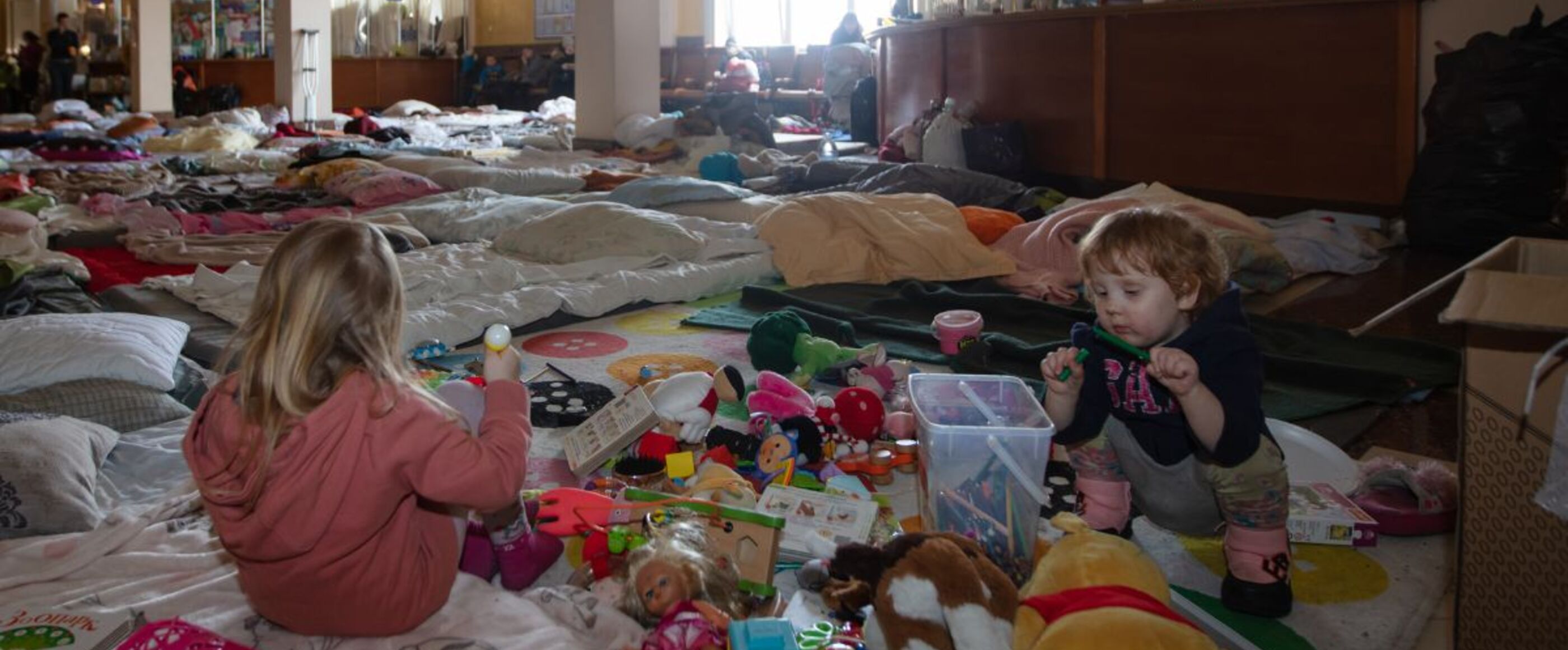 In einem Raum liegen Decken über den ganzen Boden, Kinder spielen mit Kuscheltieren und anderen Spielsachen darauf.